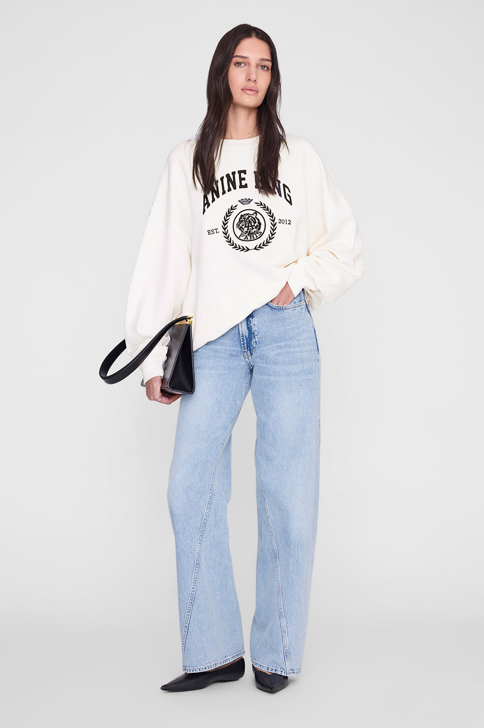 Woman wearing a white sweatshirt with a logo and light blue jeans on a white background