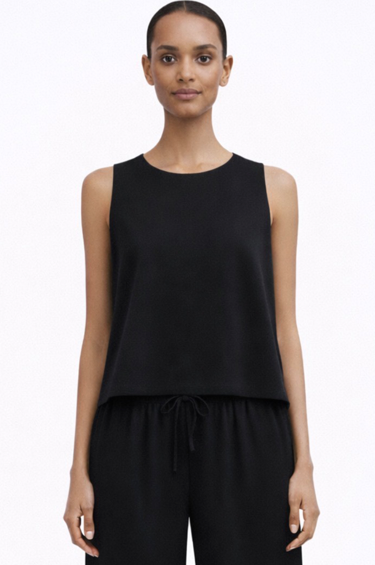 Woman wearing a black sleeveless linen top and pants on a white background