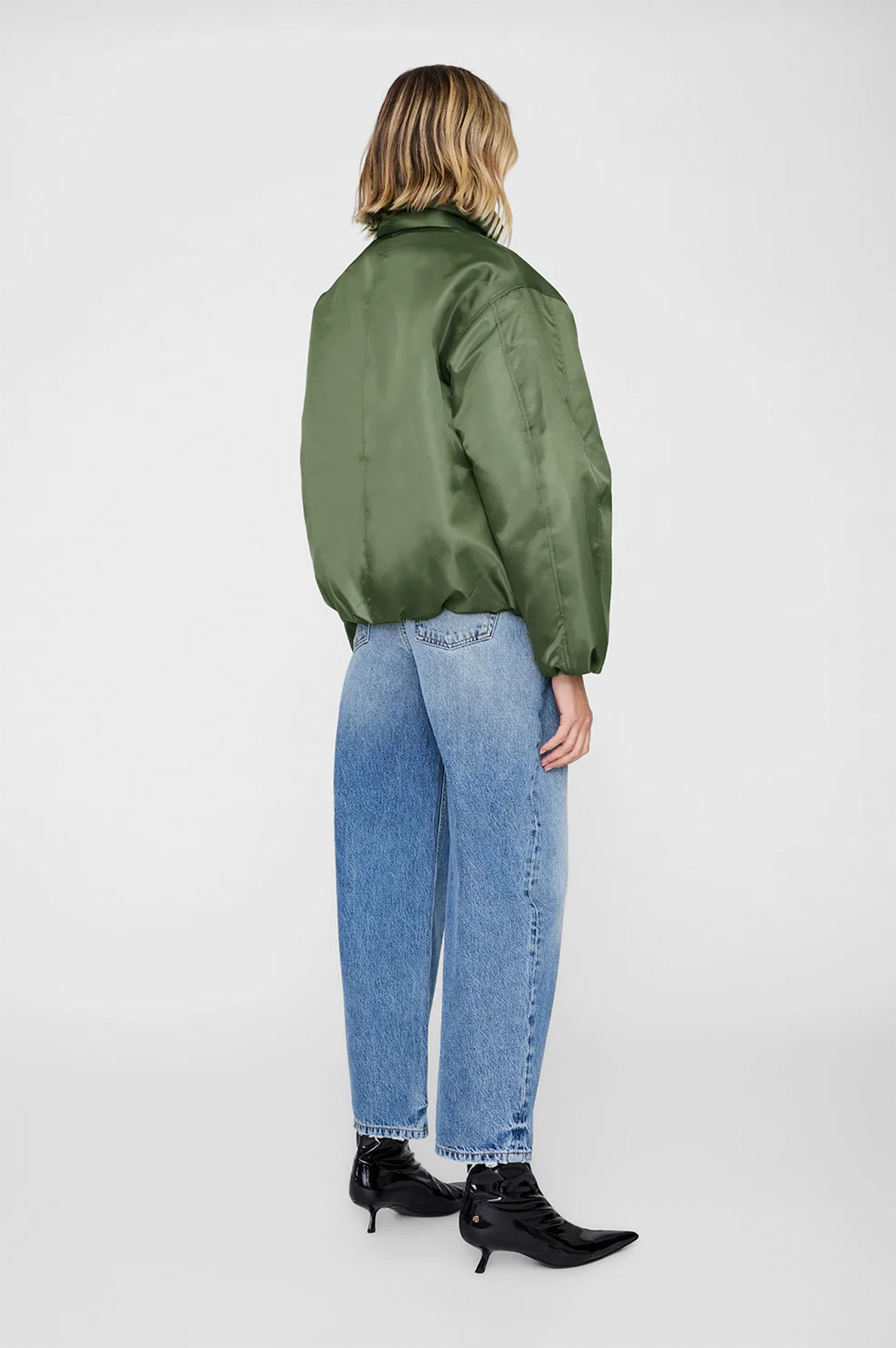 Person wearing a green satin bomber jacket and blue jeans on a white background