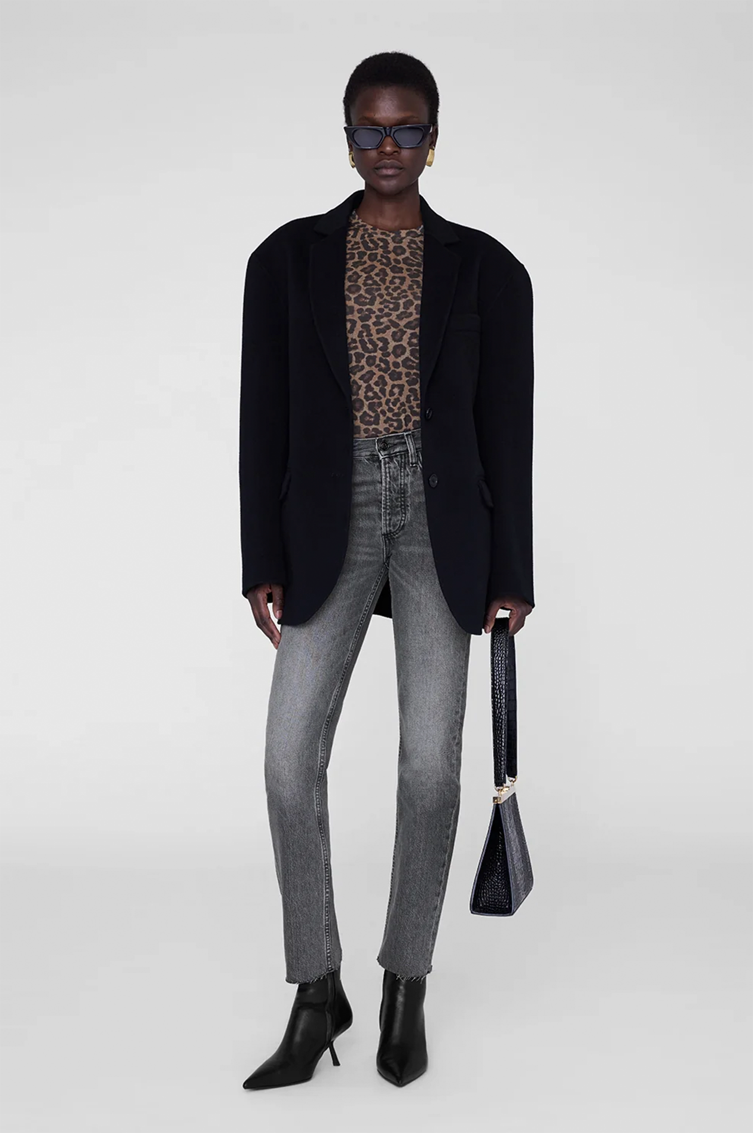 Person wearing a black coat, leopard print top, gray jeans, and black boots on a white background