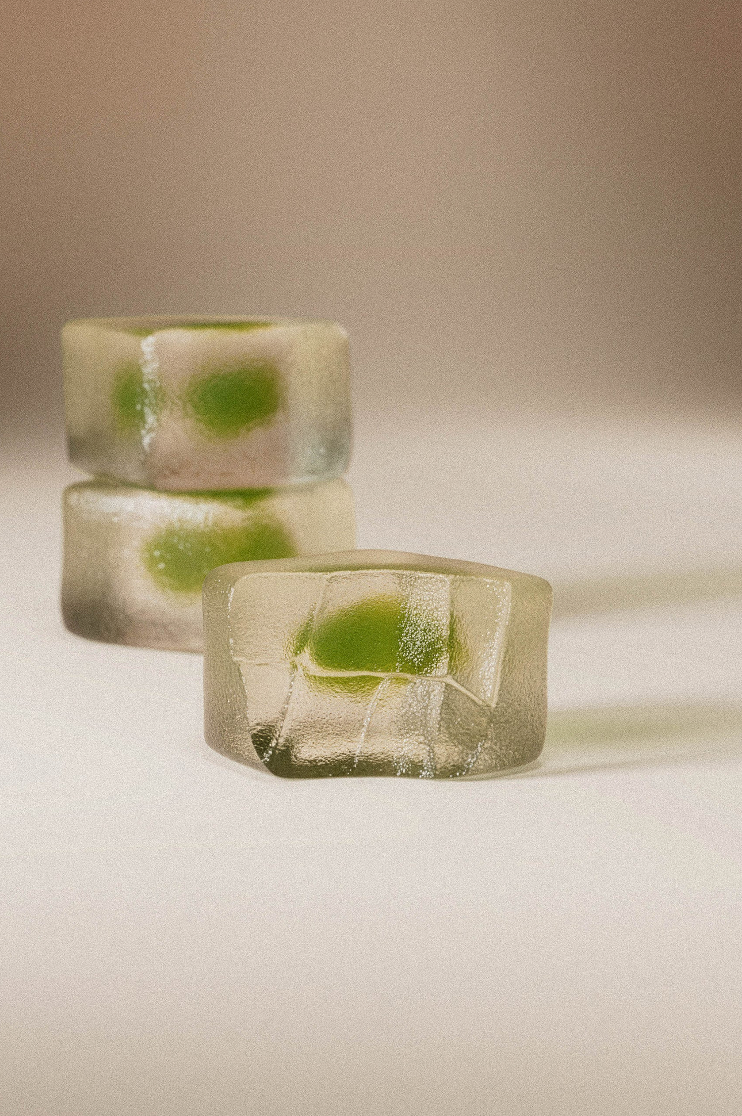 Three translucent frosted rings with green inclusions, arranged in a stack on a warm beige background.