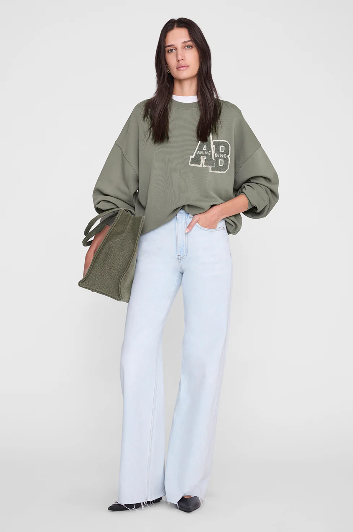Person wearing a green oversized sweatshirt with a logo and light blue jeans on a white background