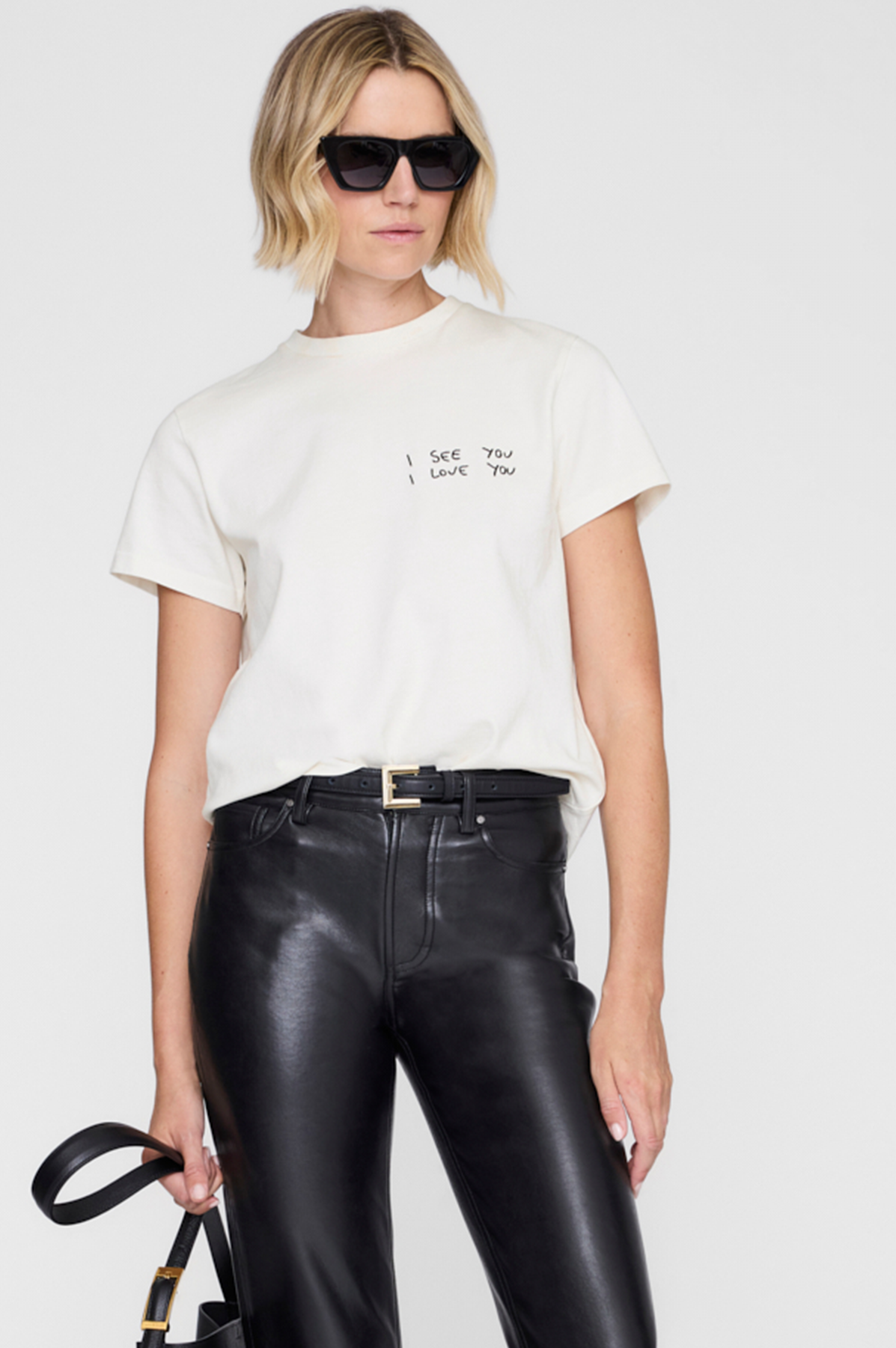 Person wearing a white t-shirt with text and black leather pants on a plain background