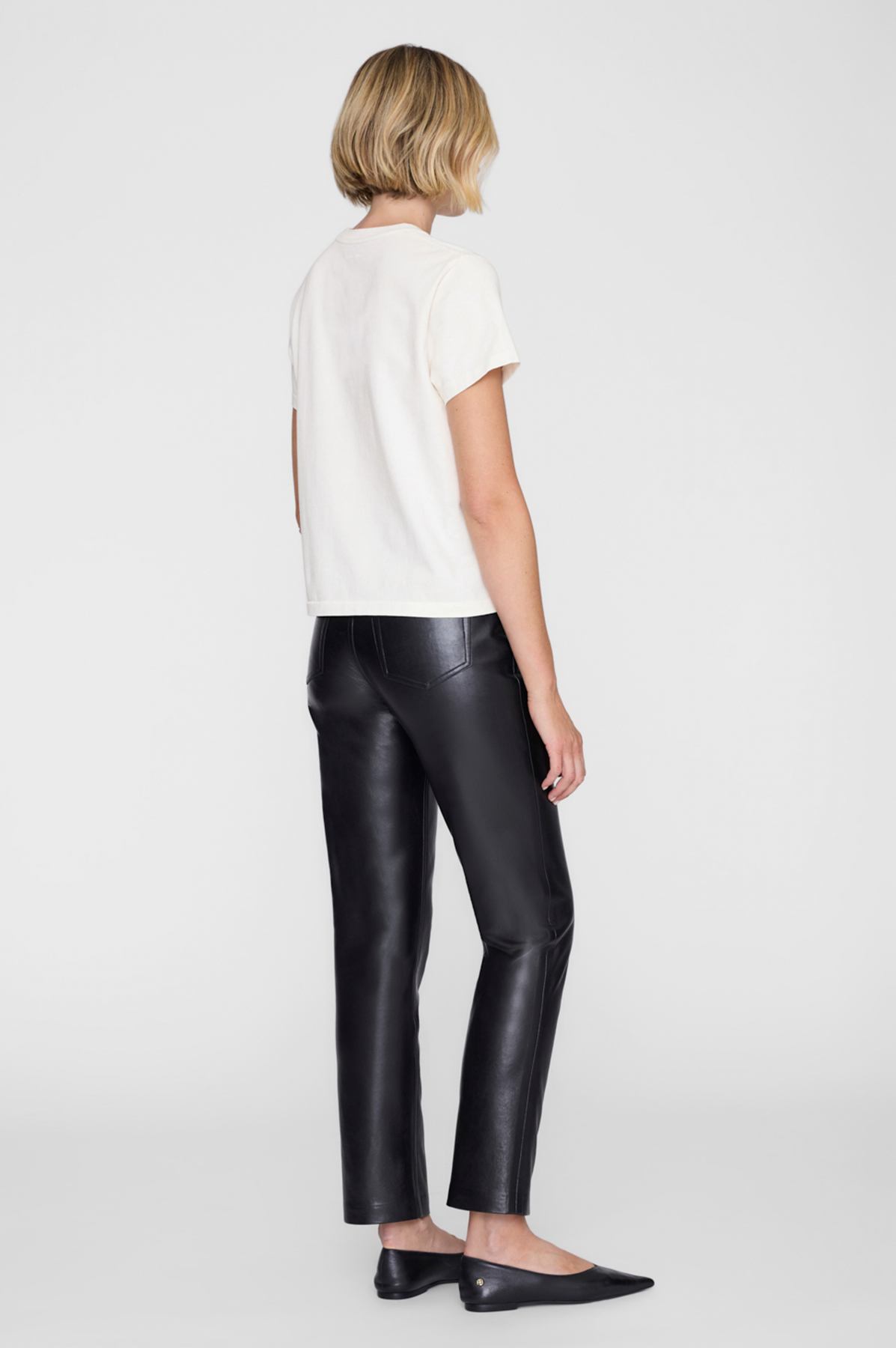 Person wearing a white top and black leather pants on a white background