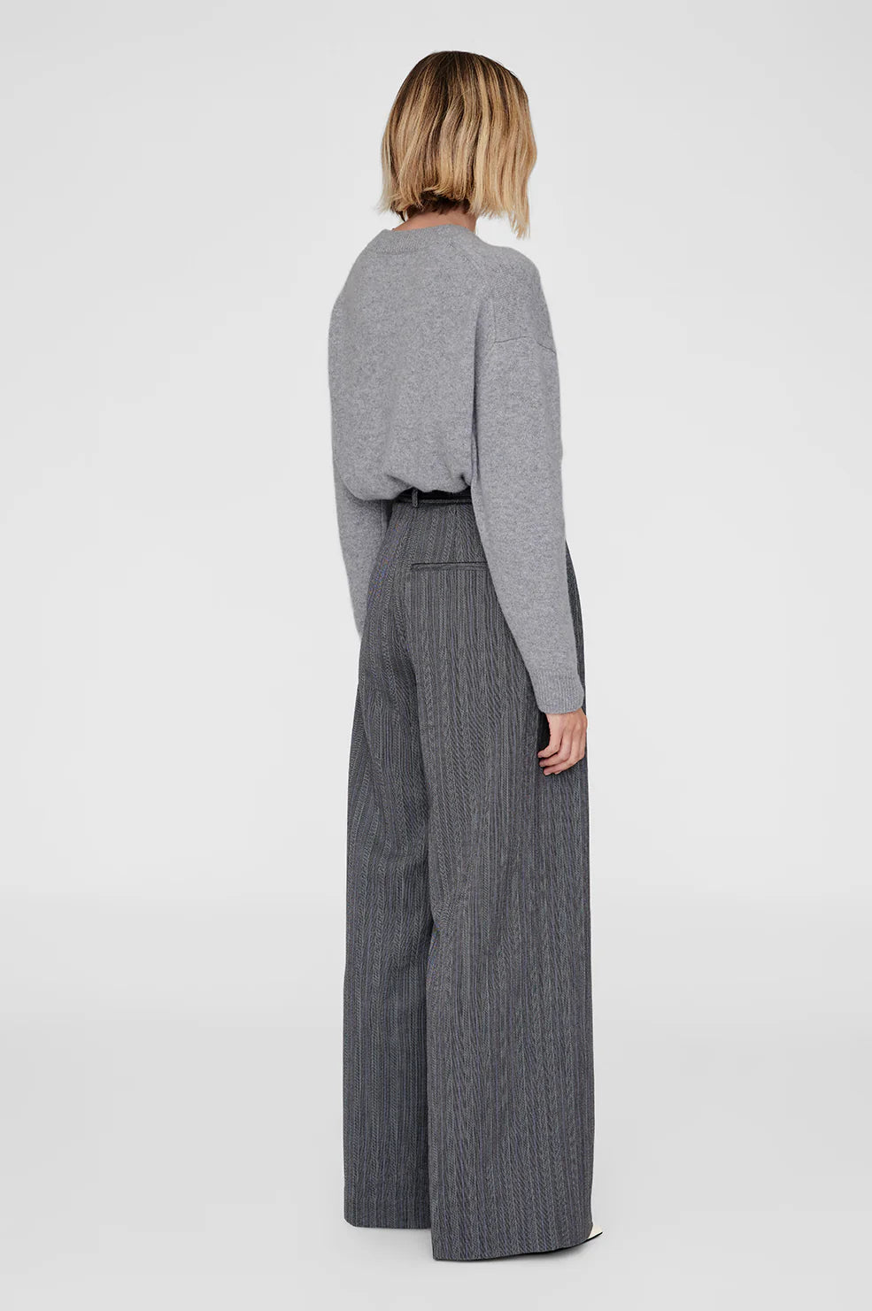 Person wearing a gray cashmere crew neck sweater and wide-leg pants on a white background