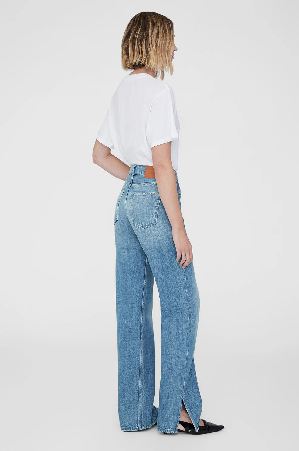 Person wearing light blue jeans and a white top on a plain background