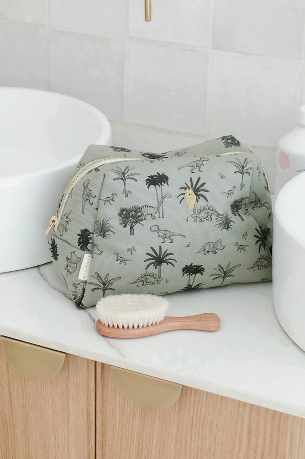 Dinosaur-patterned toiletry bag on a bathroom counter with a brush next to it.