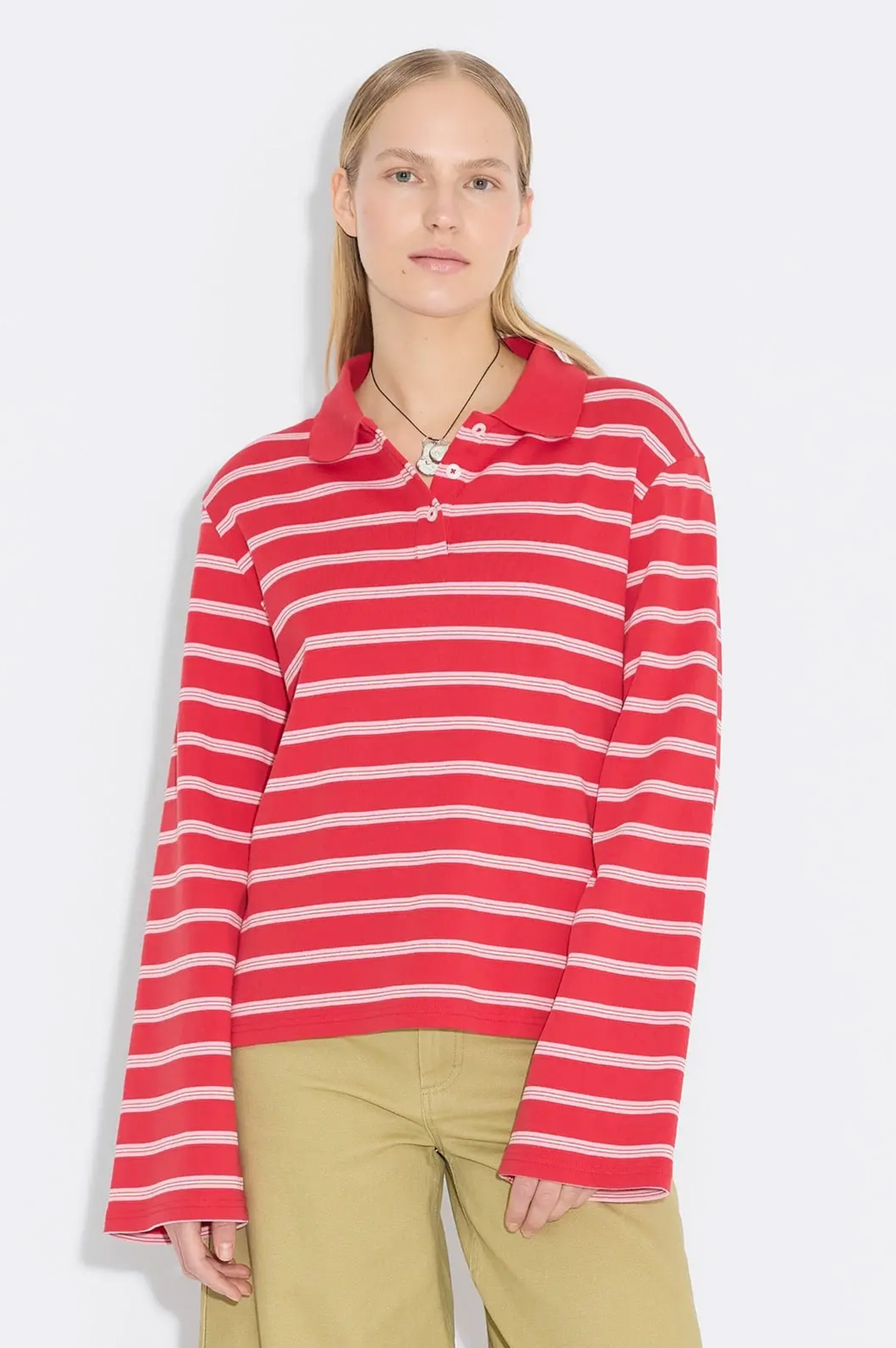A woman modeling a red and white horizontally striped long-sleeve knit polo shirt with a collar, paired with khaki pants, against a light gray studio background.
