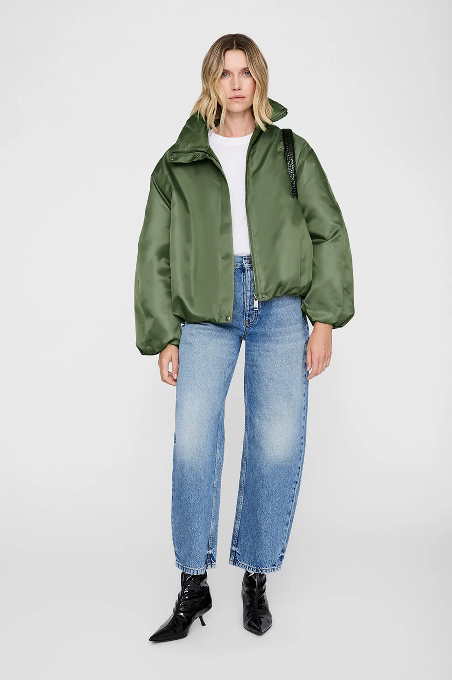 Person wearing a green jacket, white shirt, blue jeans, and black boots on a white background