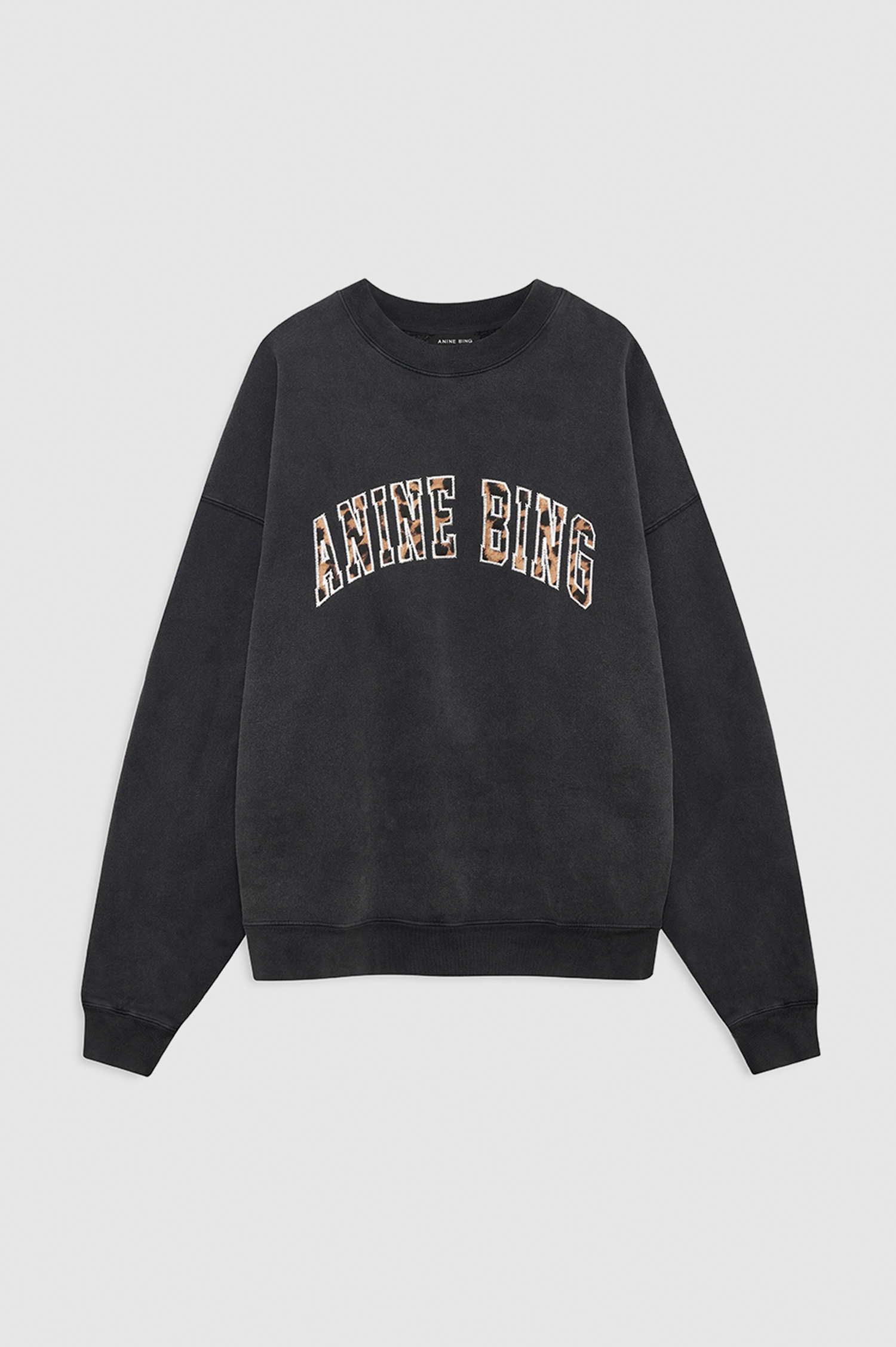 A black crewneck sweatshirt with 'ANNE BING' printed in arched varsity letters across the chest, featuring a textured beige and brown patterned fill inside the lettering. The sweatshirt is displayed flat against a light gray background.
