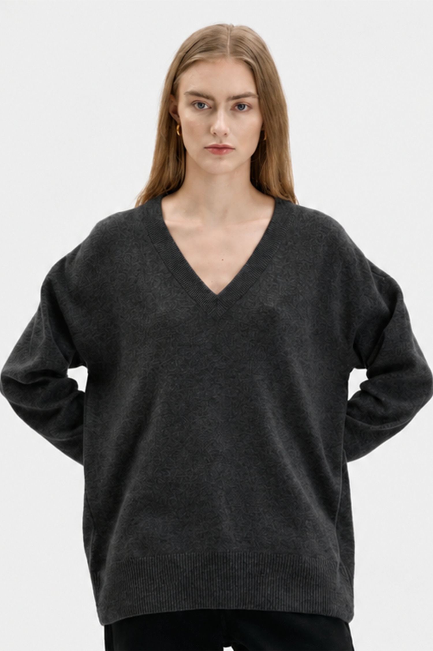 A woman modeling an oversized dark charcoal gray V-neck cashmere knit sweater against a plain light gray studio background.