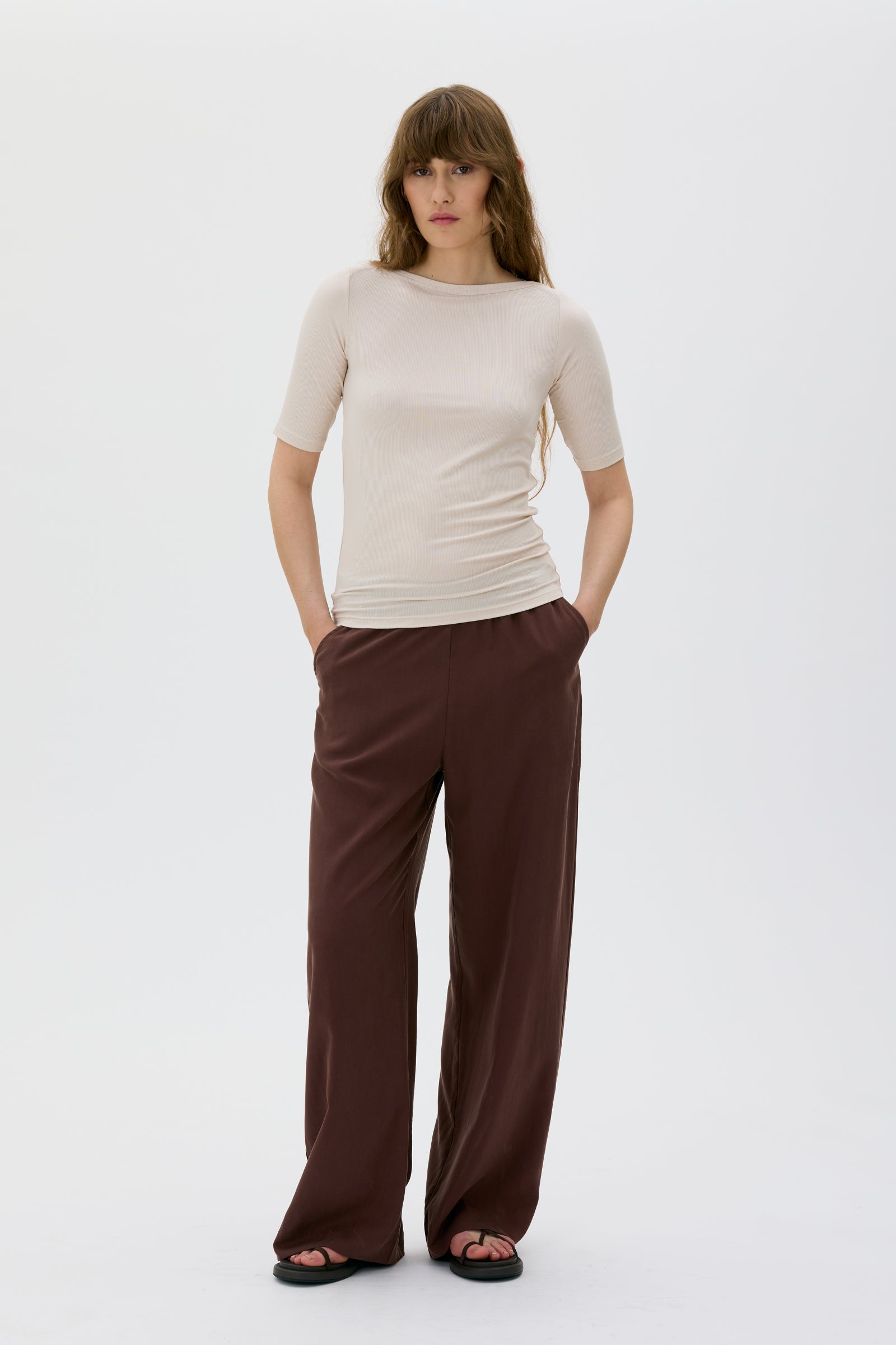 Woman wearing a beige top and brown pants on a white background