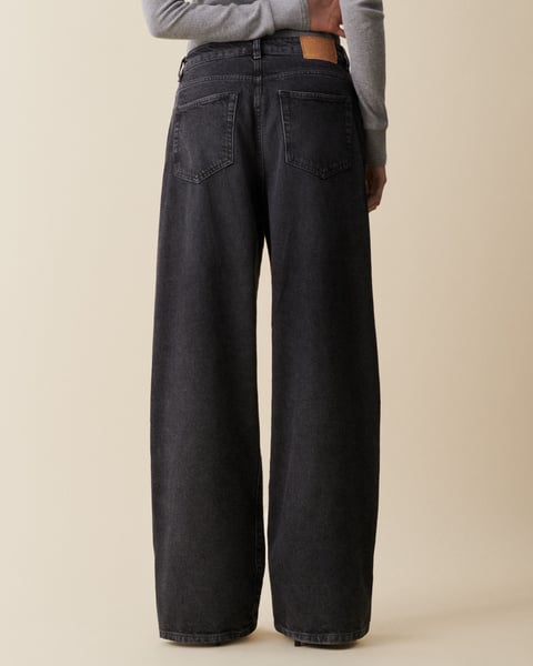 Black wide-leg jeans worn by a person on a beige background