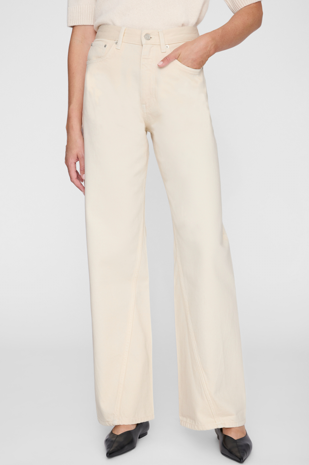 Person wearing cream-colored wide-leg jeans on a plain background