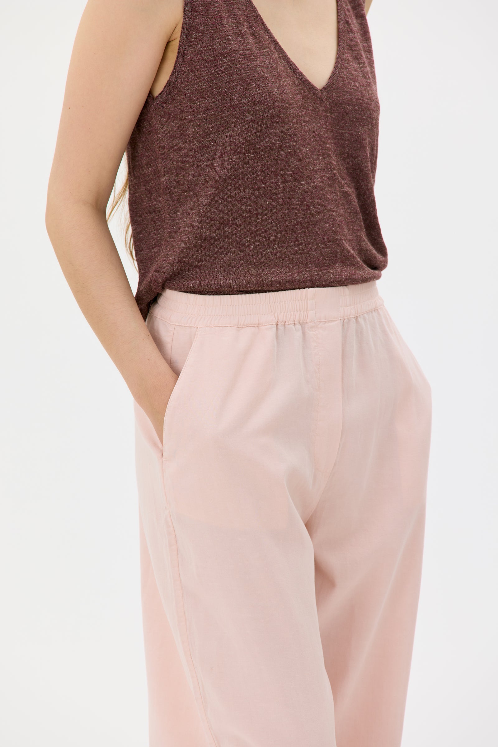 Person wearing a brown sleeveless top and light pink pants on a white background