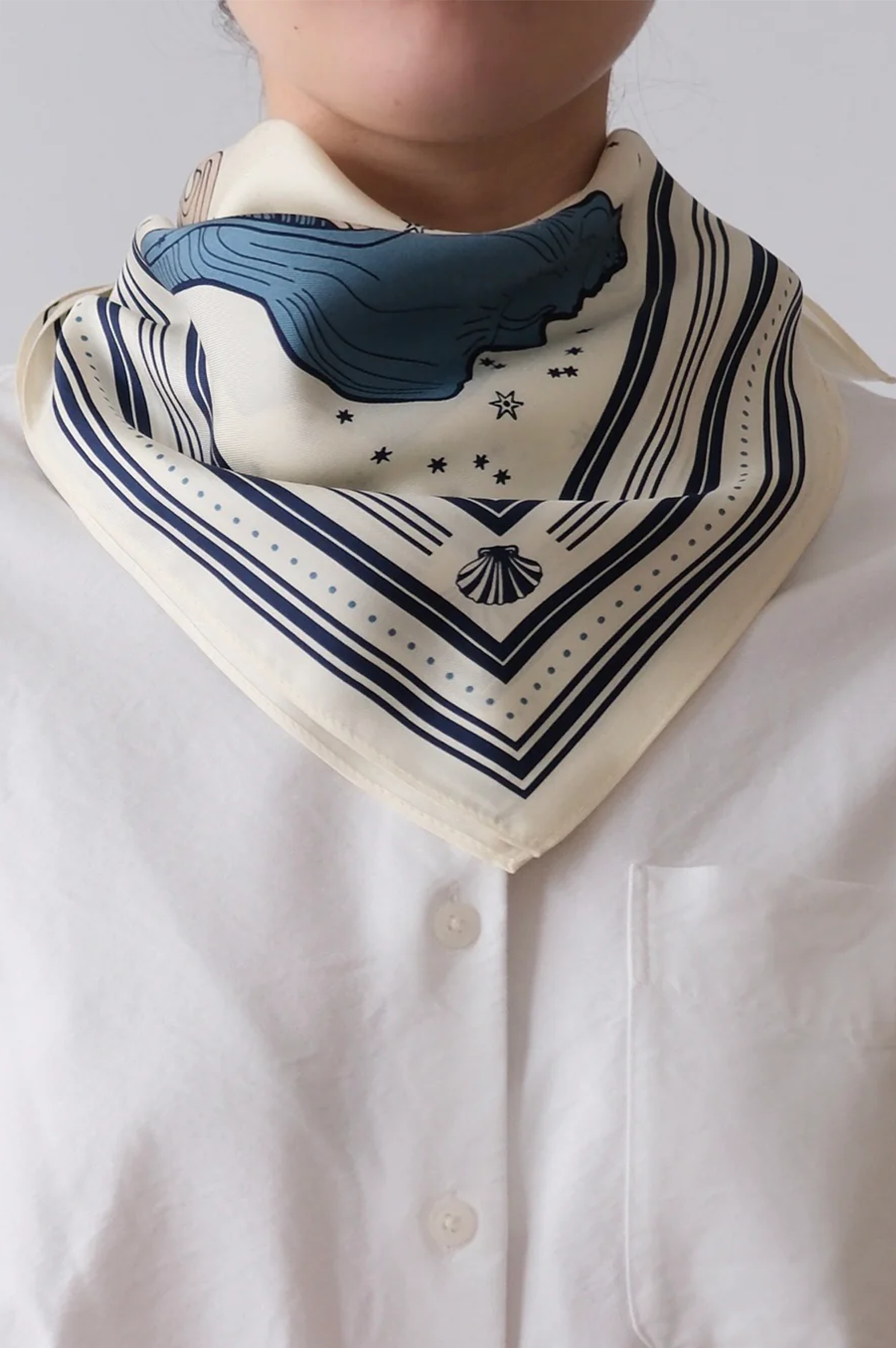 Person wearing a white shirt with a decorative blue and black patterned scarf.