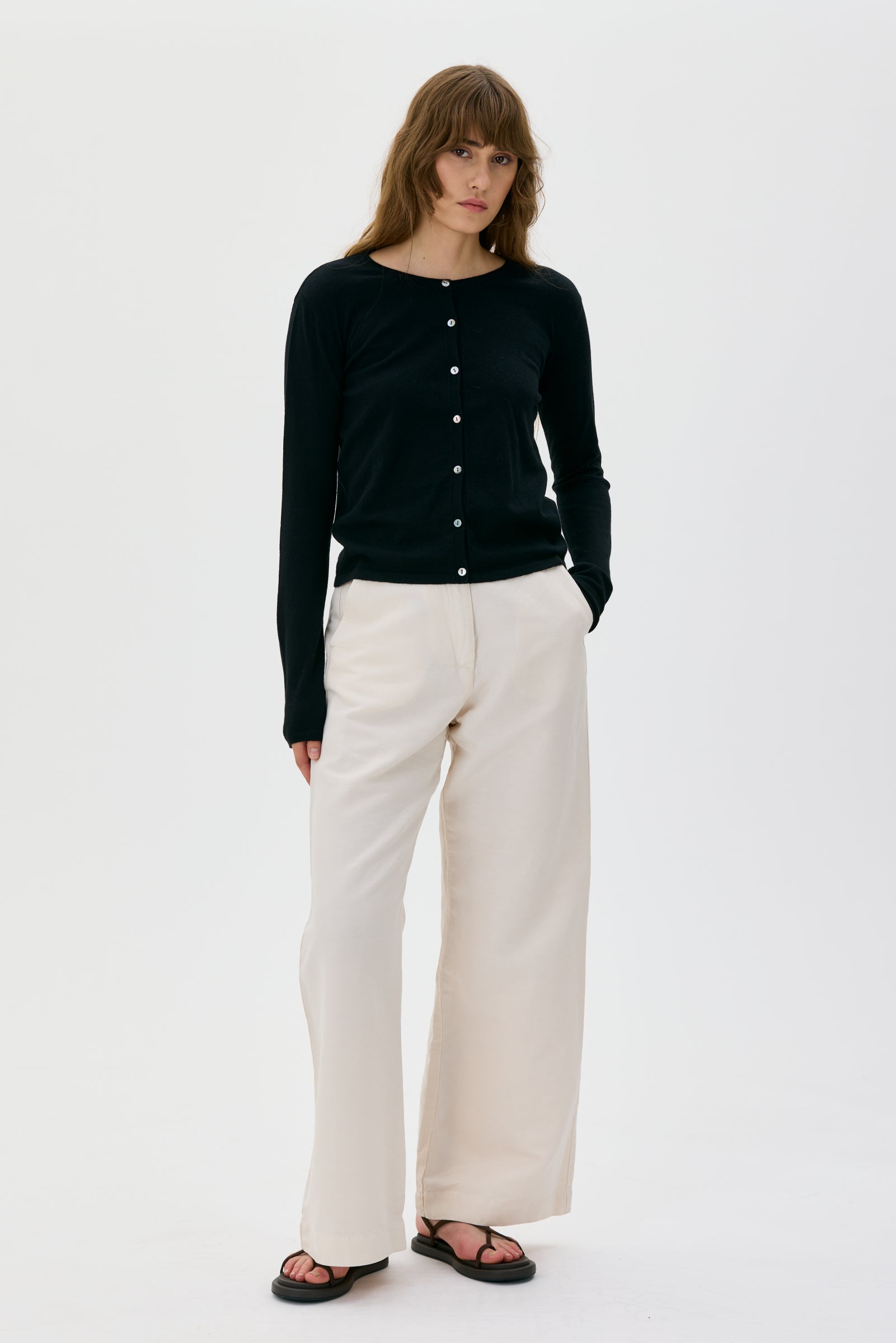 Woman wearing a black Lidia cardigan from Maska and white pants on a white background