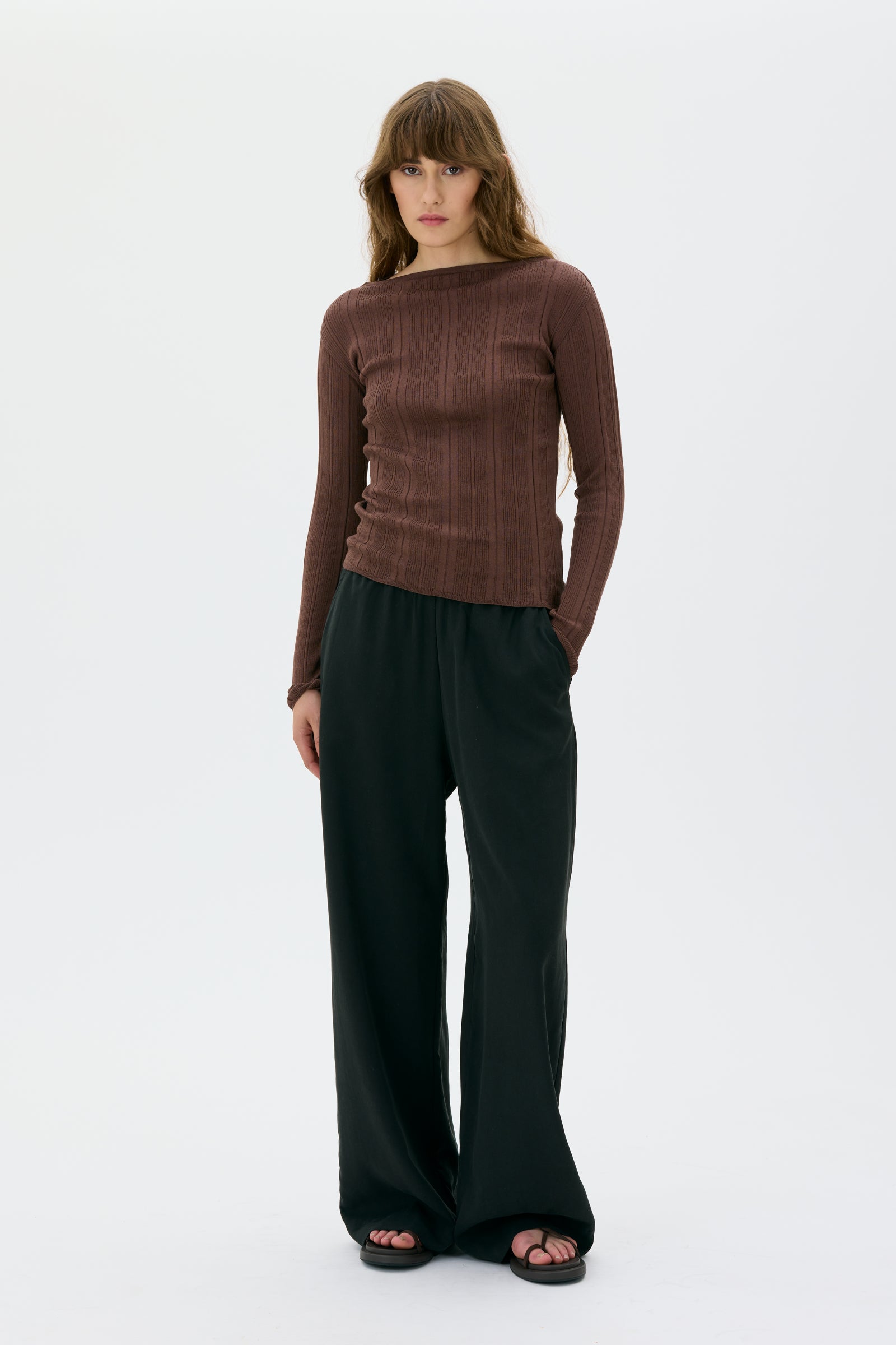 Woman wearing a brown long-sleeve top in organic fabric from maska and black pants on a white background 