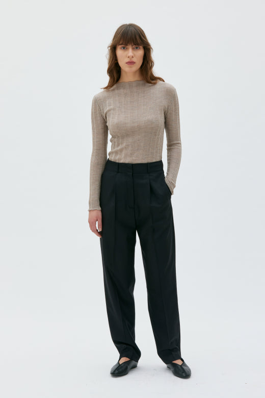Woman wearing a beige long-sleeve top and black pants on a white background