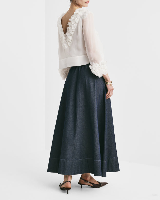 Woman wearing a white blouse with ruffled details and a dark blue skirt on a light gray background