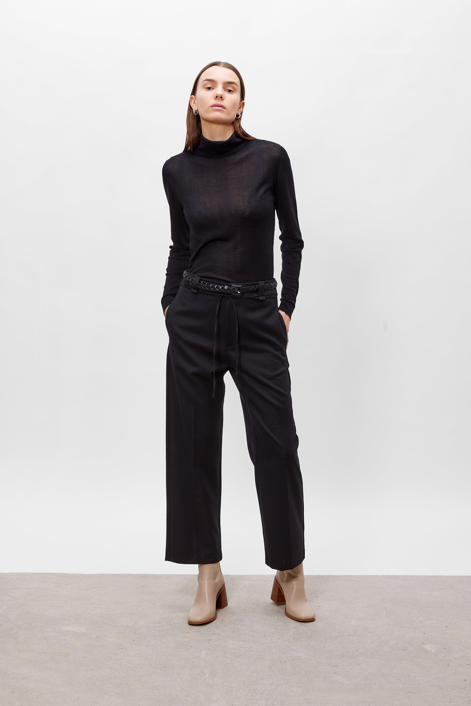 Person wearing a black turtleneck and black pants on a white background
