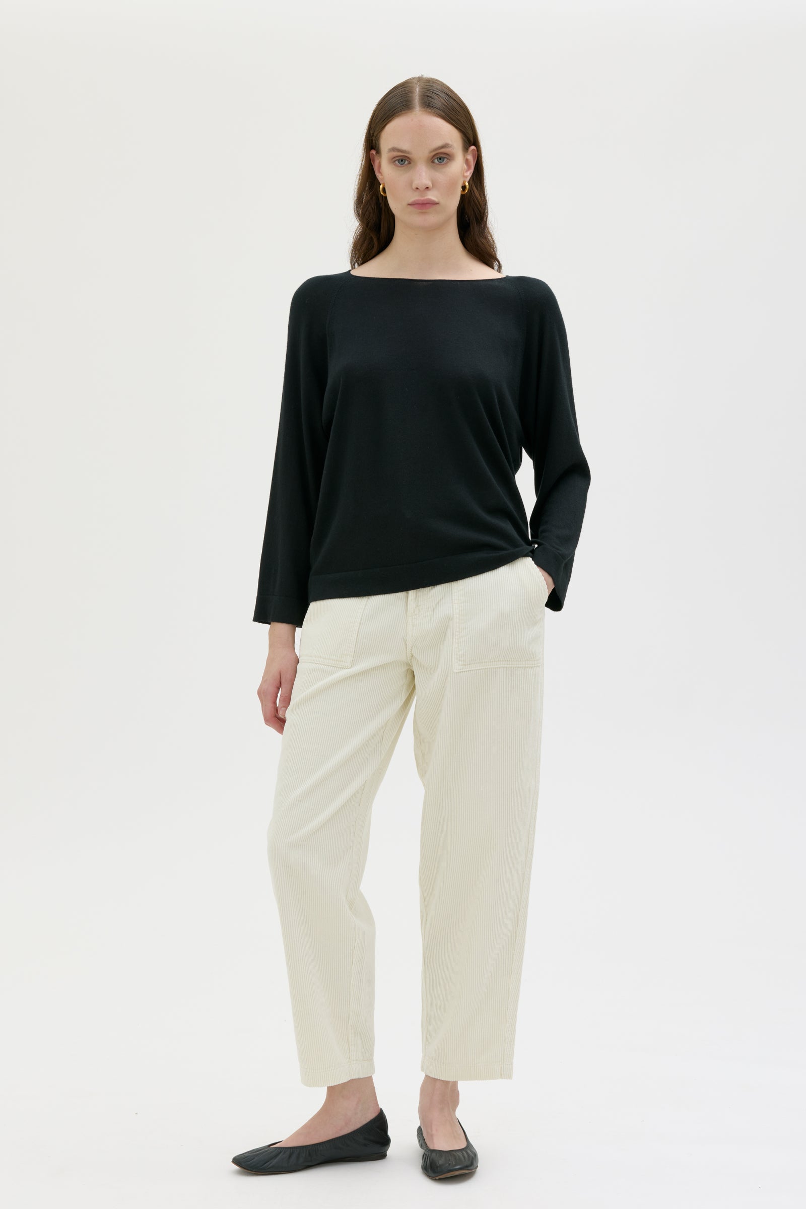 Woman wearing a black cashmere and silk top from maska and white pants on a white background