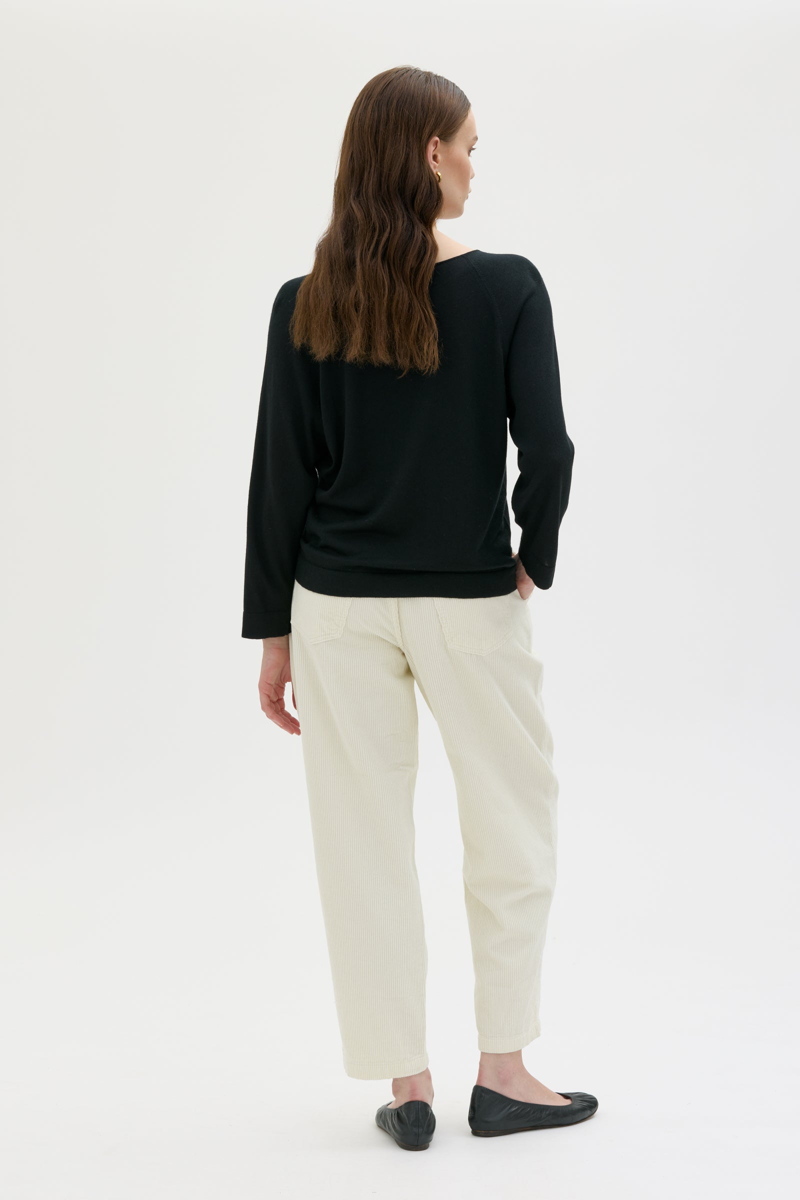 Person wearing a black knitted cashmere top and white pants on a white background